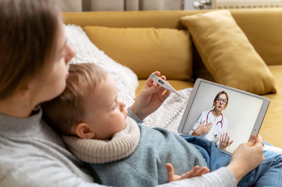mamma sul divano con bambino malato parla con il pediatra a distanza tramite la telemedicina